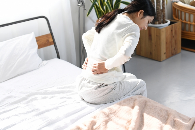起床時にベッドの上で腰を押さえる女性