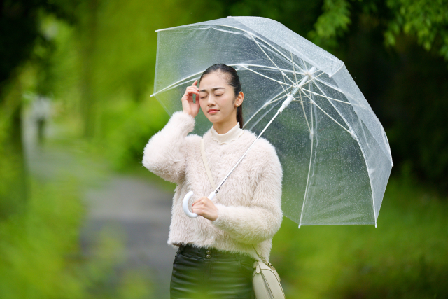 雨の日に傘を持って頭を押さえる女性